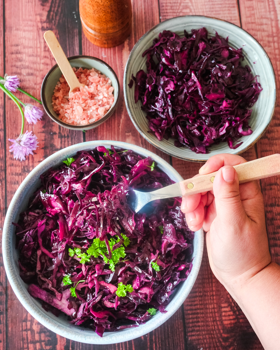 A bowl of red cabbage salad - with a hand holding a fork