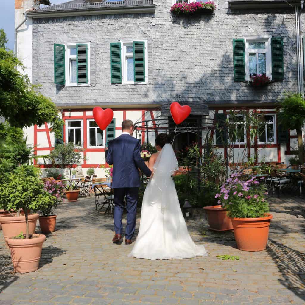 a wedding couple with the back turned to us, holding two heart shaped baloons 