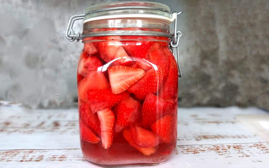 Strawberry Vodka in a Jar. The strawberries are red, the background grey and the jar stands on a white wooden background. 