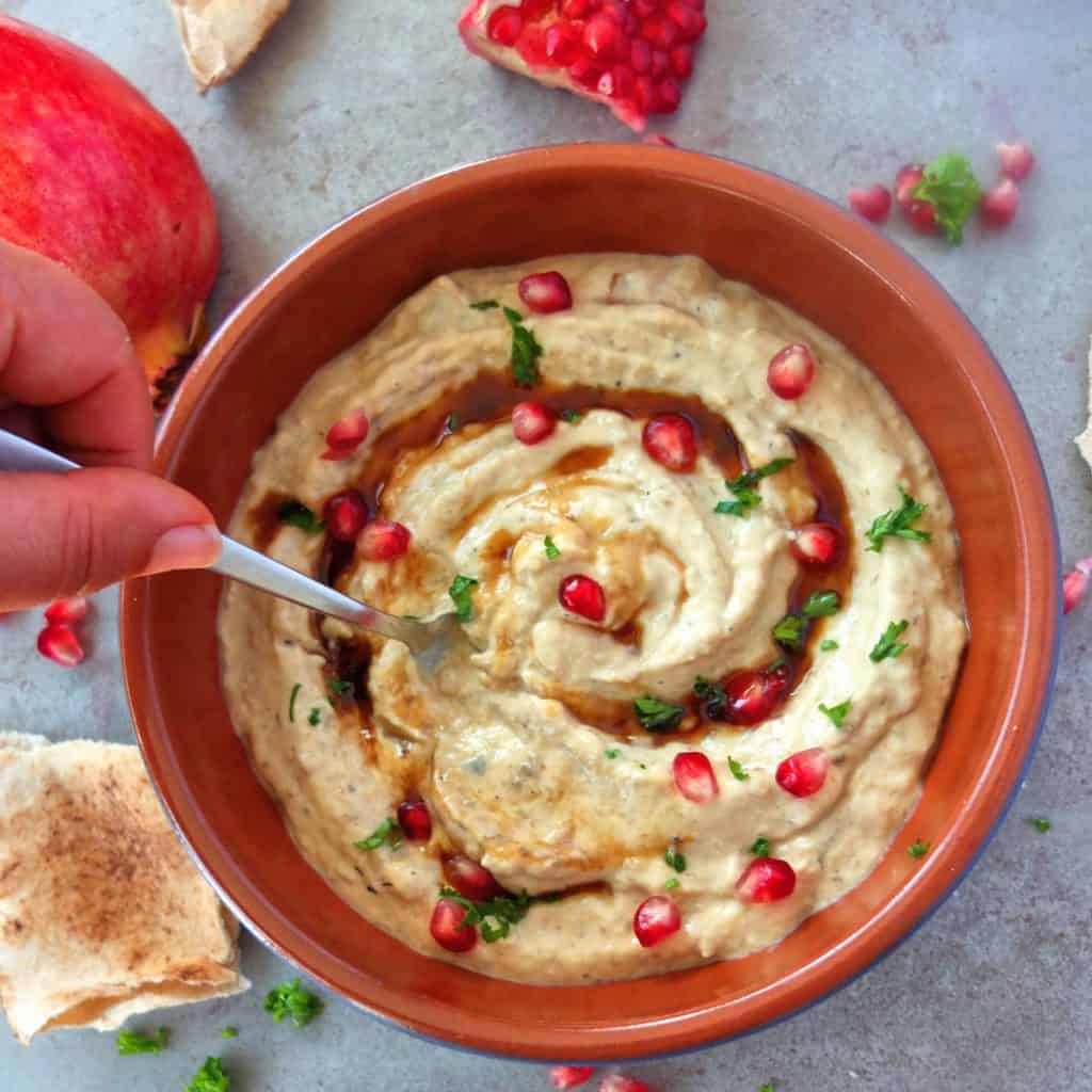 Baba Ganoush sprinkled with pomegranate seeds a hand is holding a spoon