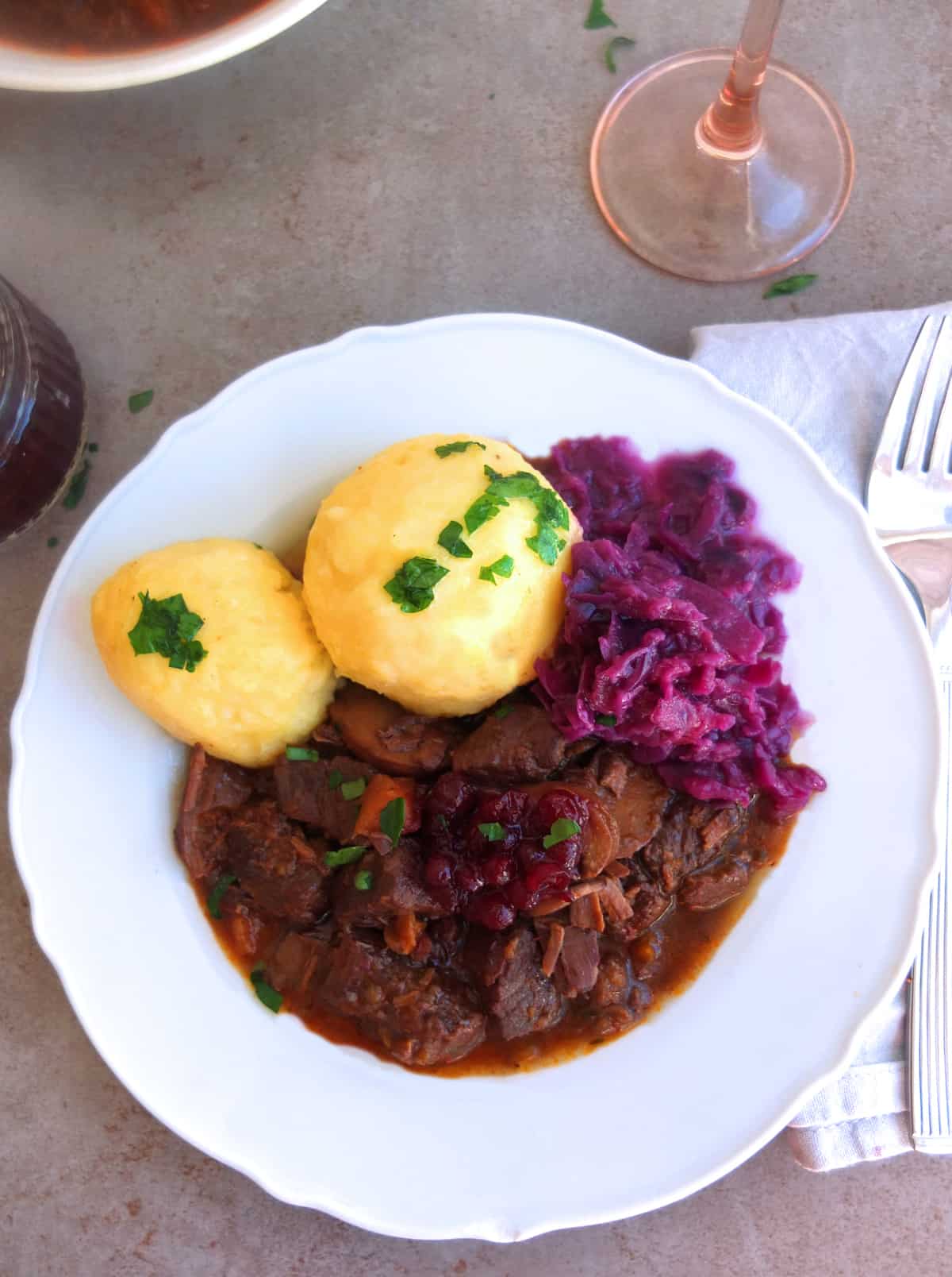 Vensions Goulash with German Potato Dumplings and Red Cabbage on a white plate with a grey background 