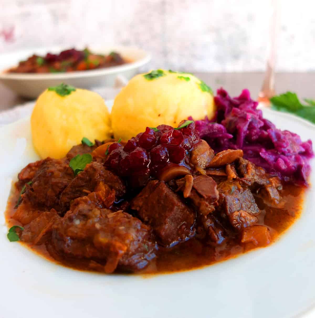 Venison Goulash on a white plate with potato dumplings and red cabbage 