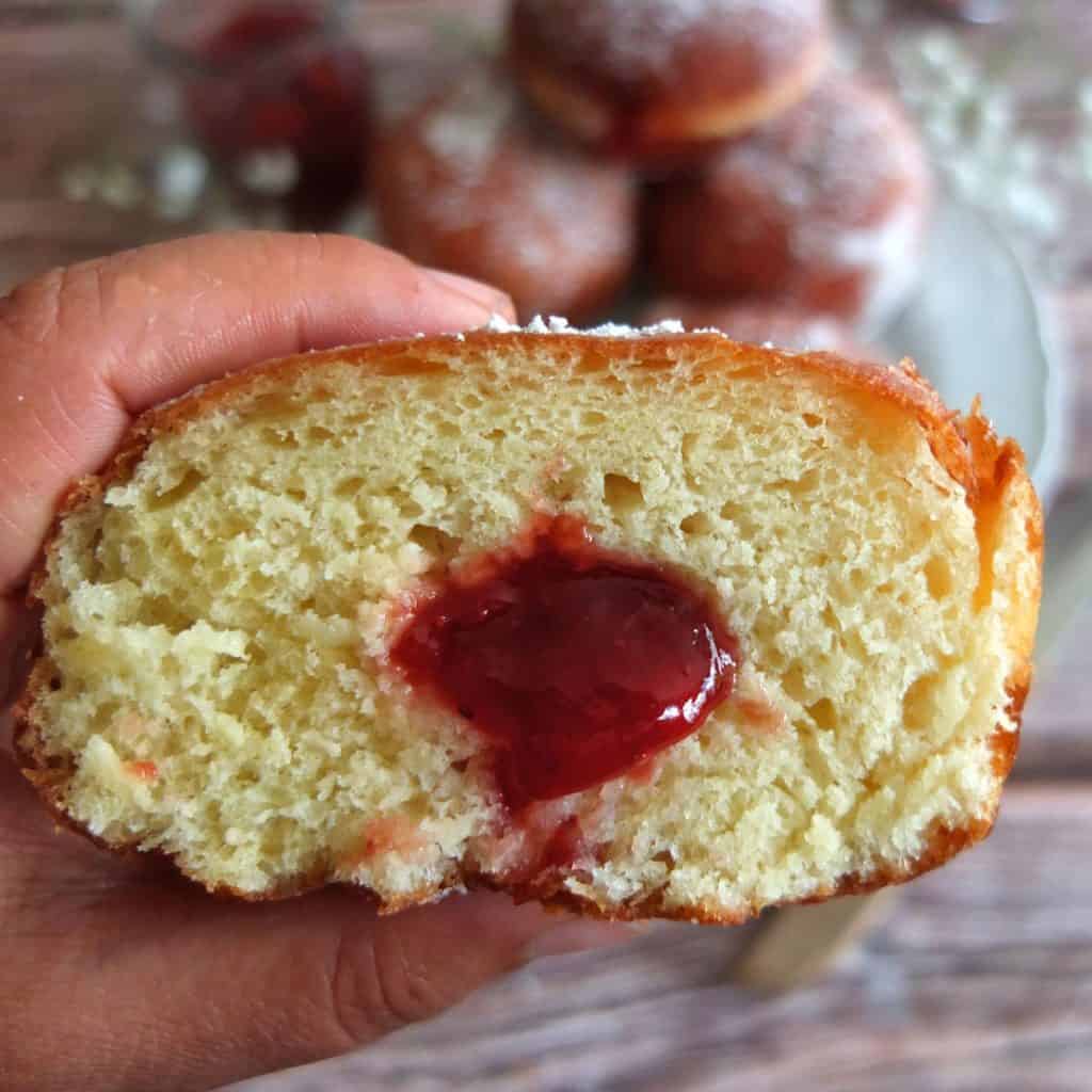 A Hand holding a Berliner that has been sliced in half. You can see the jam in the middle