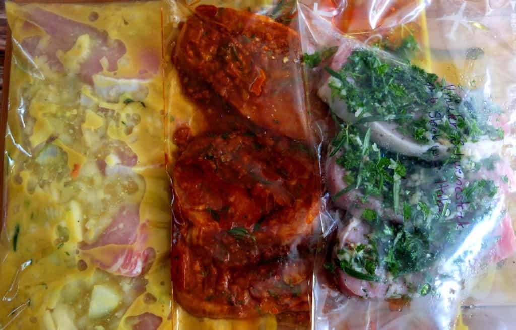 Pork steaks in zipper bags in three marinades: yellow is a mustard marinade, red is a paprika marinade and green is a herb marinade. 