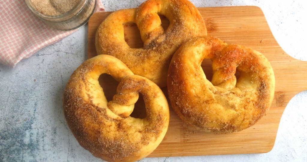 Sugar pretzels on a chopping board. Above you can see part of a bowl with cinnamon sugar
