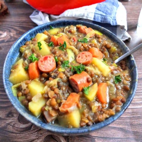 German Lentil Soup with potatoes in a blue bowl. A spoon is in the bowl