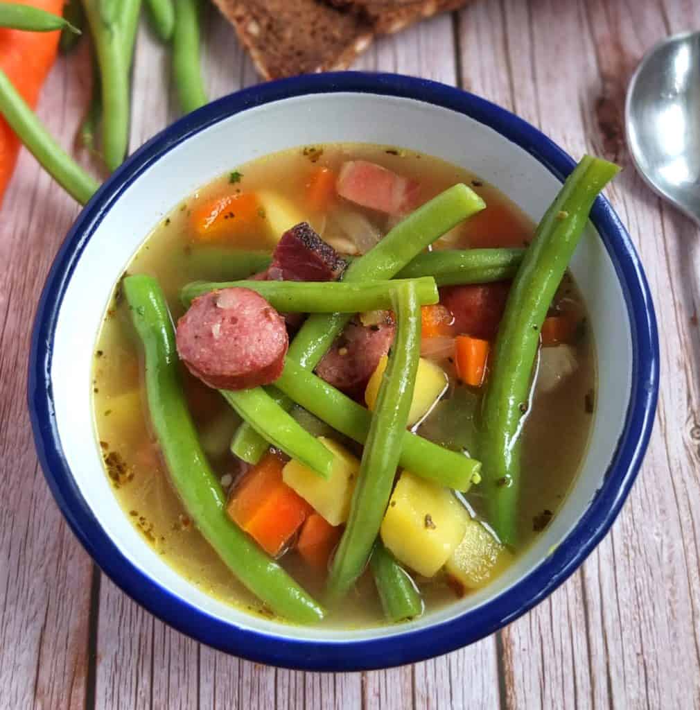 a blue and white bowl with green bean soup with sausages
