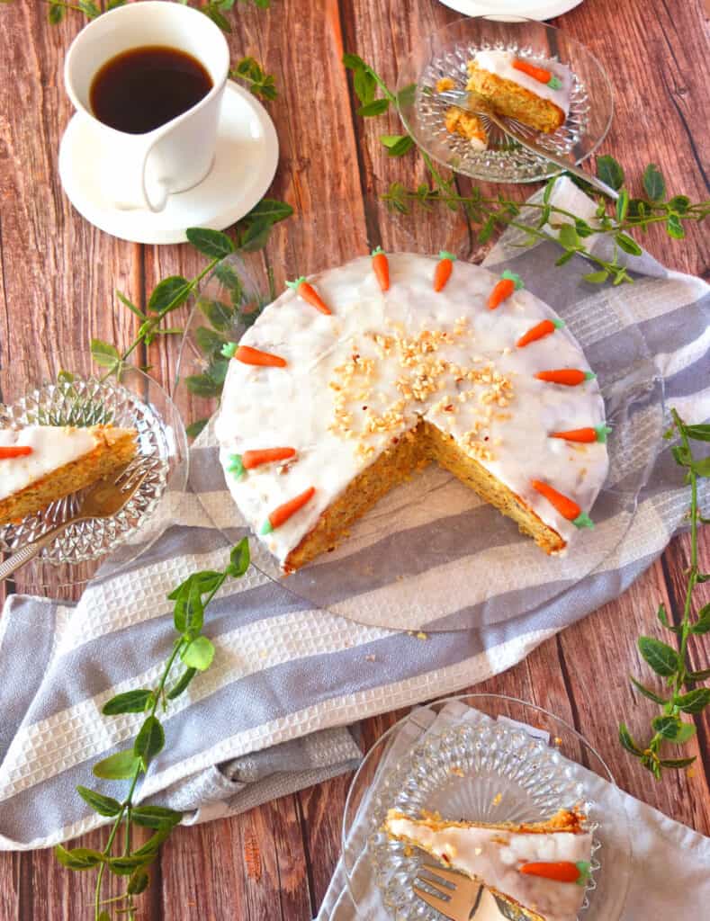 A cut open Swiss Carrot cake with slices of cake spread around. The plates are set on a wooden surface.