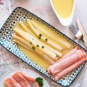 A plate with white asparagus in hollandaise sauce and ham.