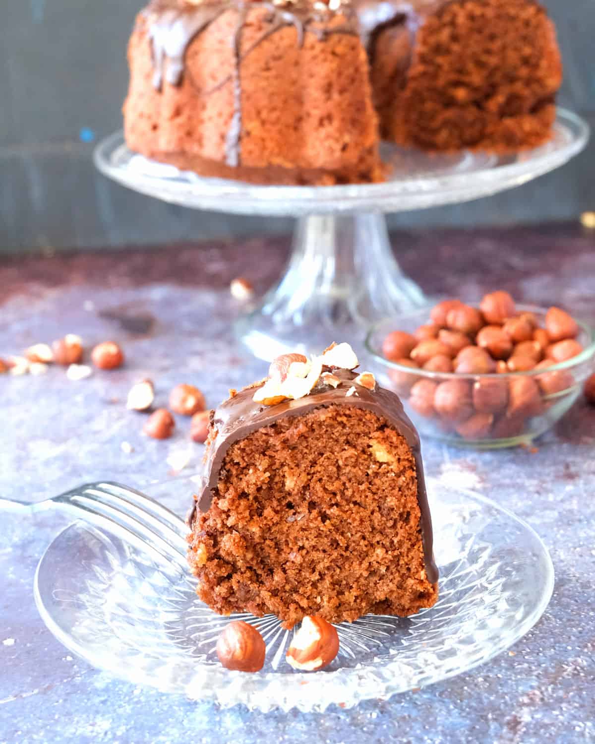 A piece of chocolate nut cake with hazelnuts in the background.