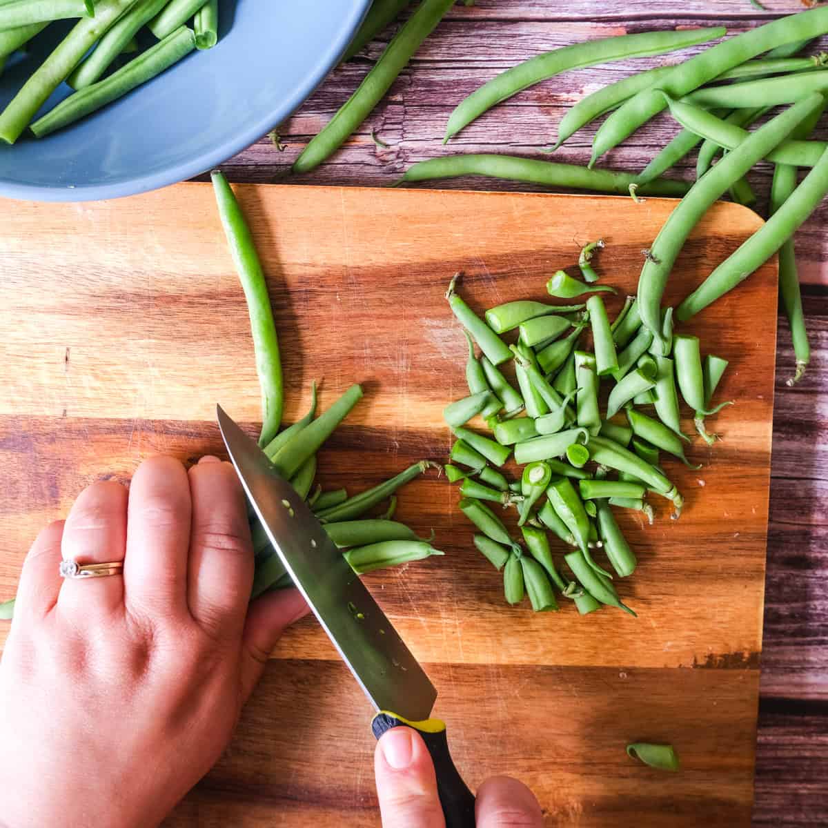 A person cutting up green beans on a cutting board.