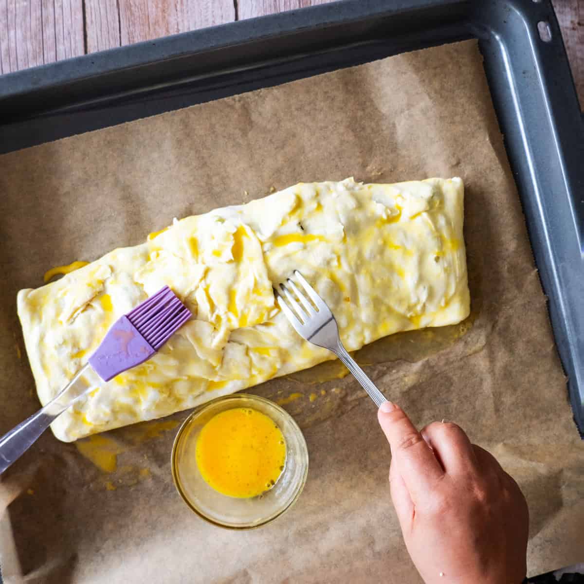 making vegetable strudel. Covering the strudel dough in egg yolk and pricking the puff pastry sheets with a fork.