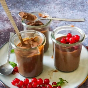 three glasses of chocolate puddings with red currants