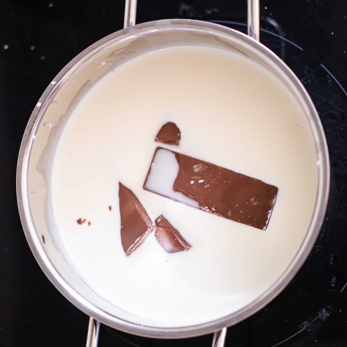 a saucepan melting chocolate bits in milk and cream for chocolate pudding