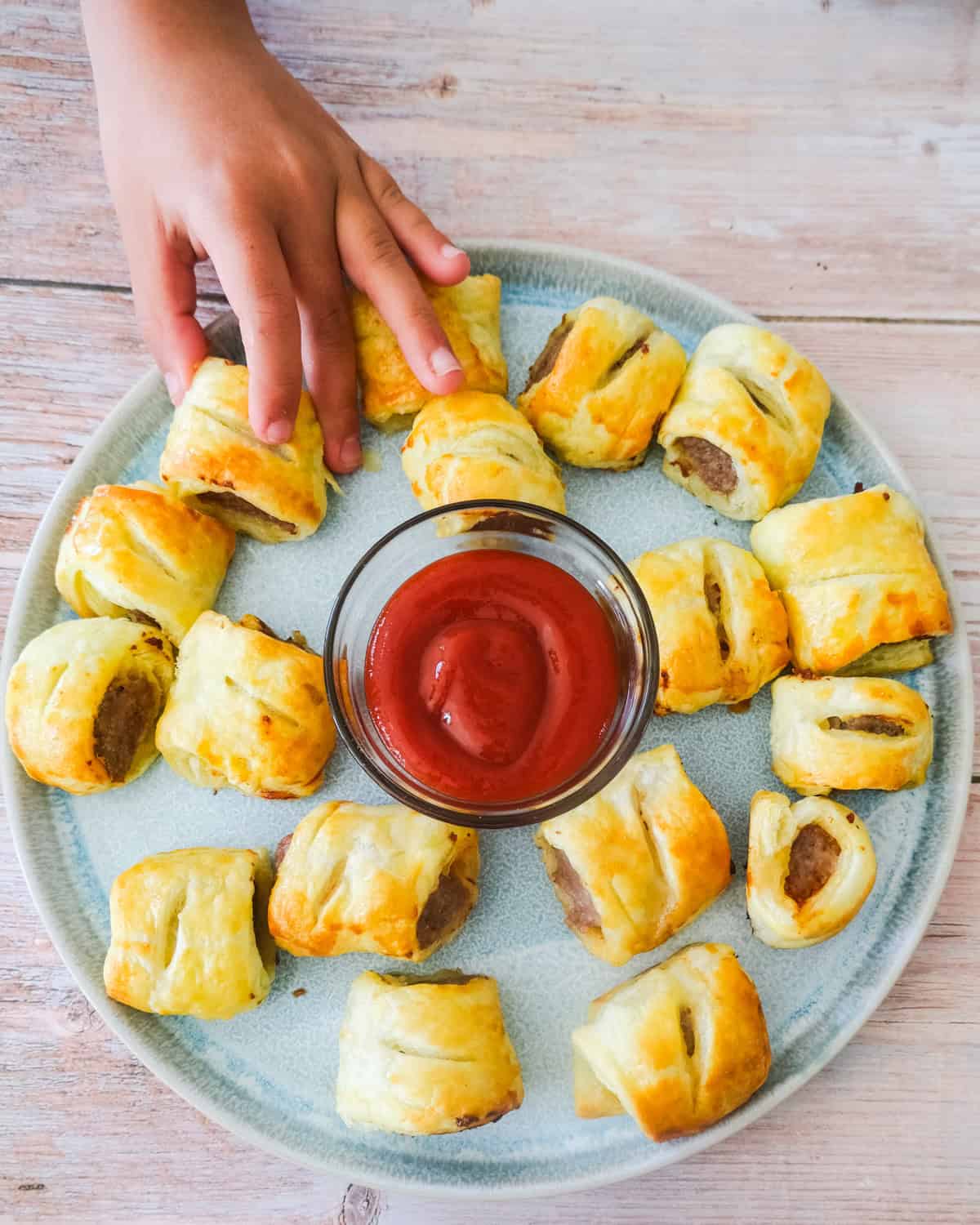a hand reaching for a german sausage roll on a platter.